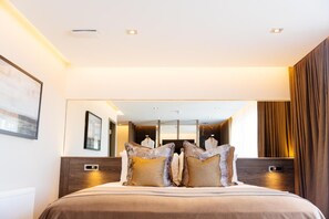 A modern hotel room with a large bed, a mirror, and a view of the room's interior.