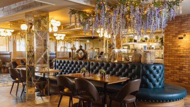 A restaurant with a wooden dining table, black leather booth seating, hanging purple flowers, and a brick wall. - The Redhurst Hotel (Glasgow)