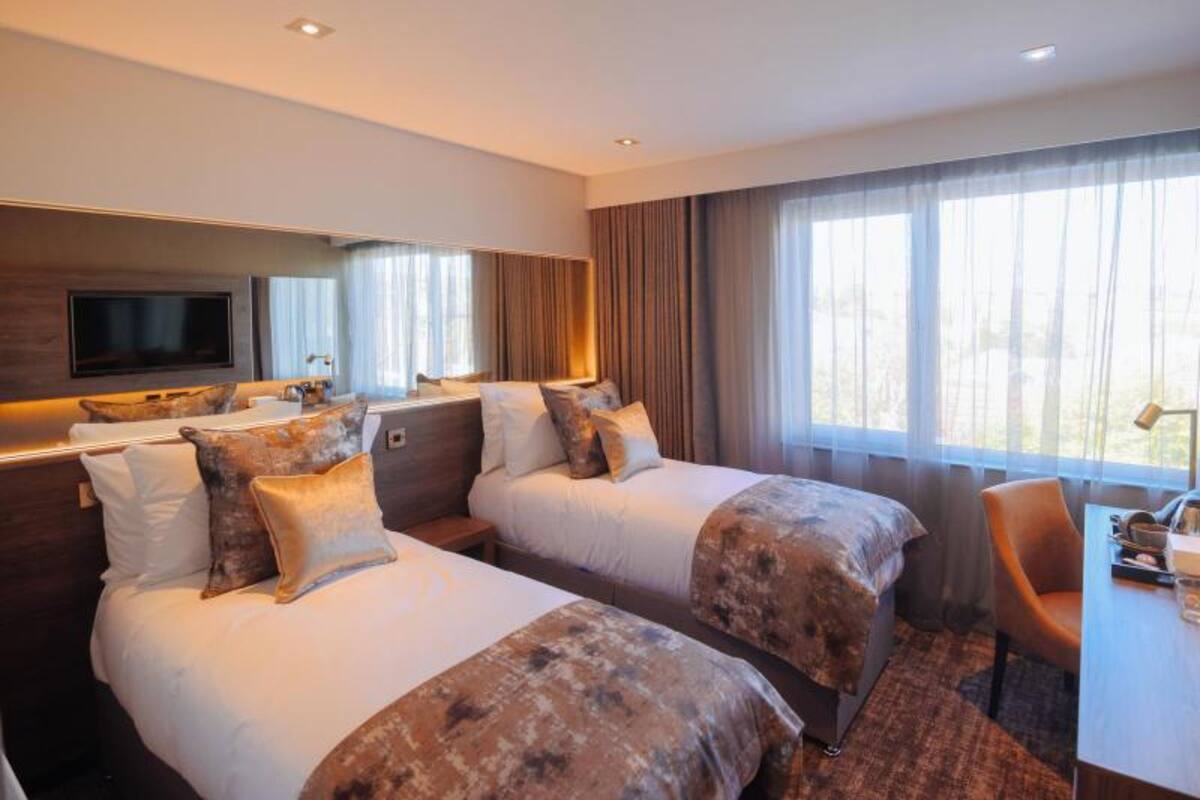 A hotel room with two beds, a TV, a desk, and a large window.