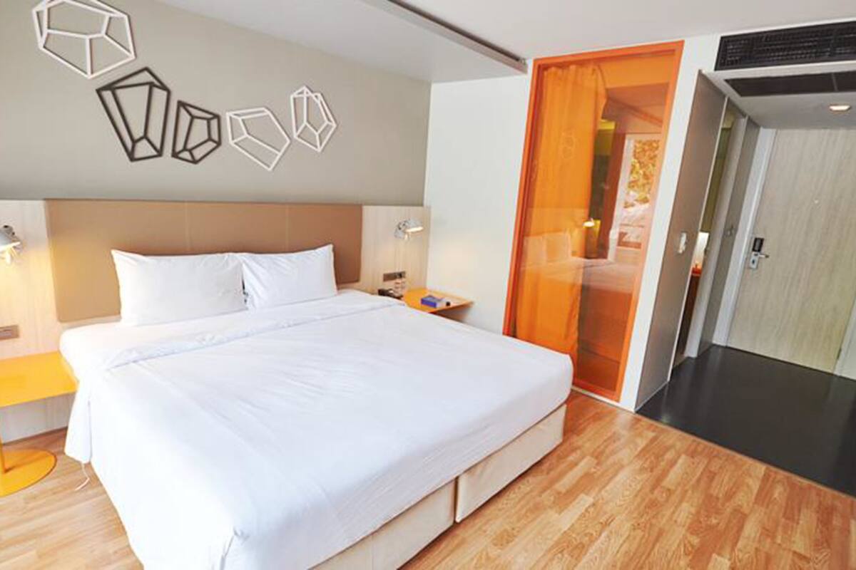 Habitación de hotel con una cama grande, suelo de madera, un armario y una puerta que da a otra habitación.