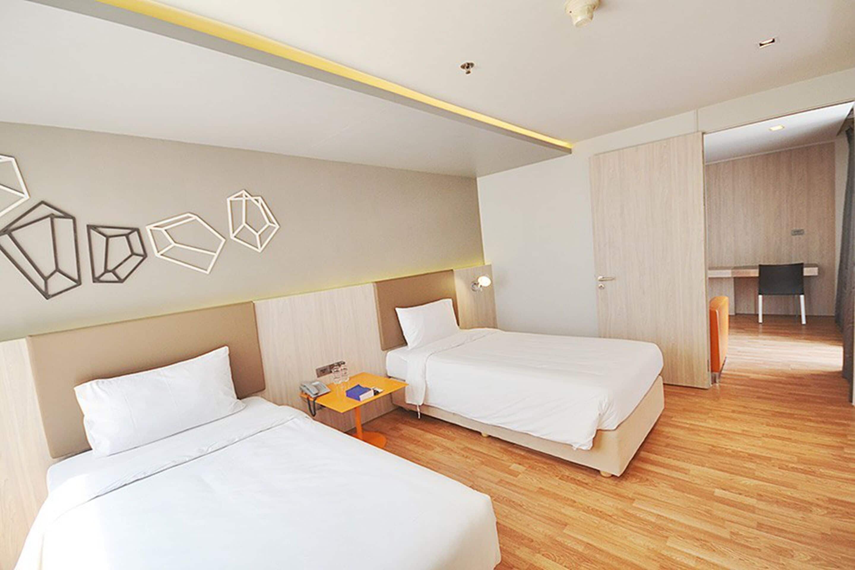 A hotel room with two beds, a small table with a phone and a book, and a desk with a chair.