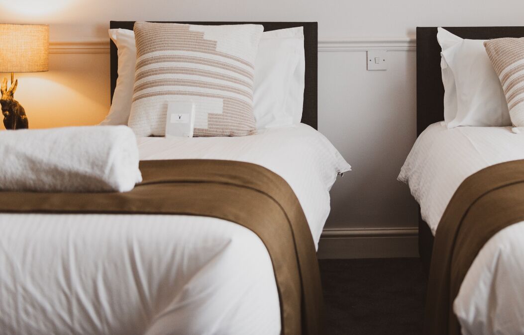 Two adjacent beds with white bedding and brown headboards, a bedside lamp, and a small decorative item on the left side.