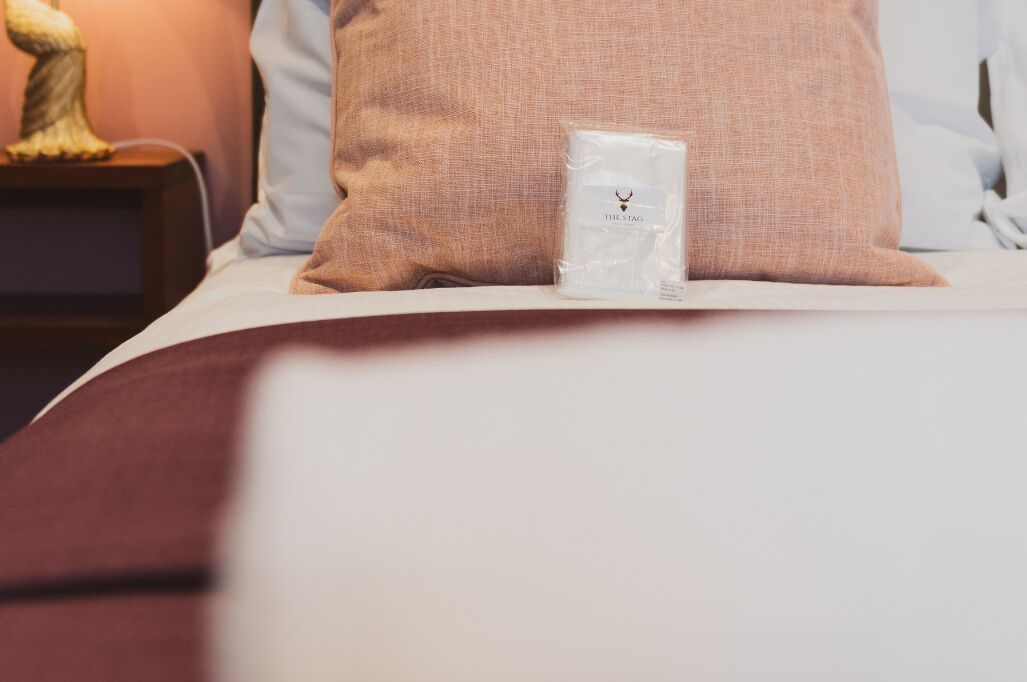 A neatly made bed with a white pillow and a small white box labeled "THE STAG" on the bed.