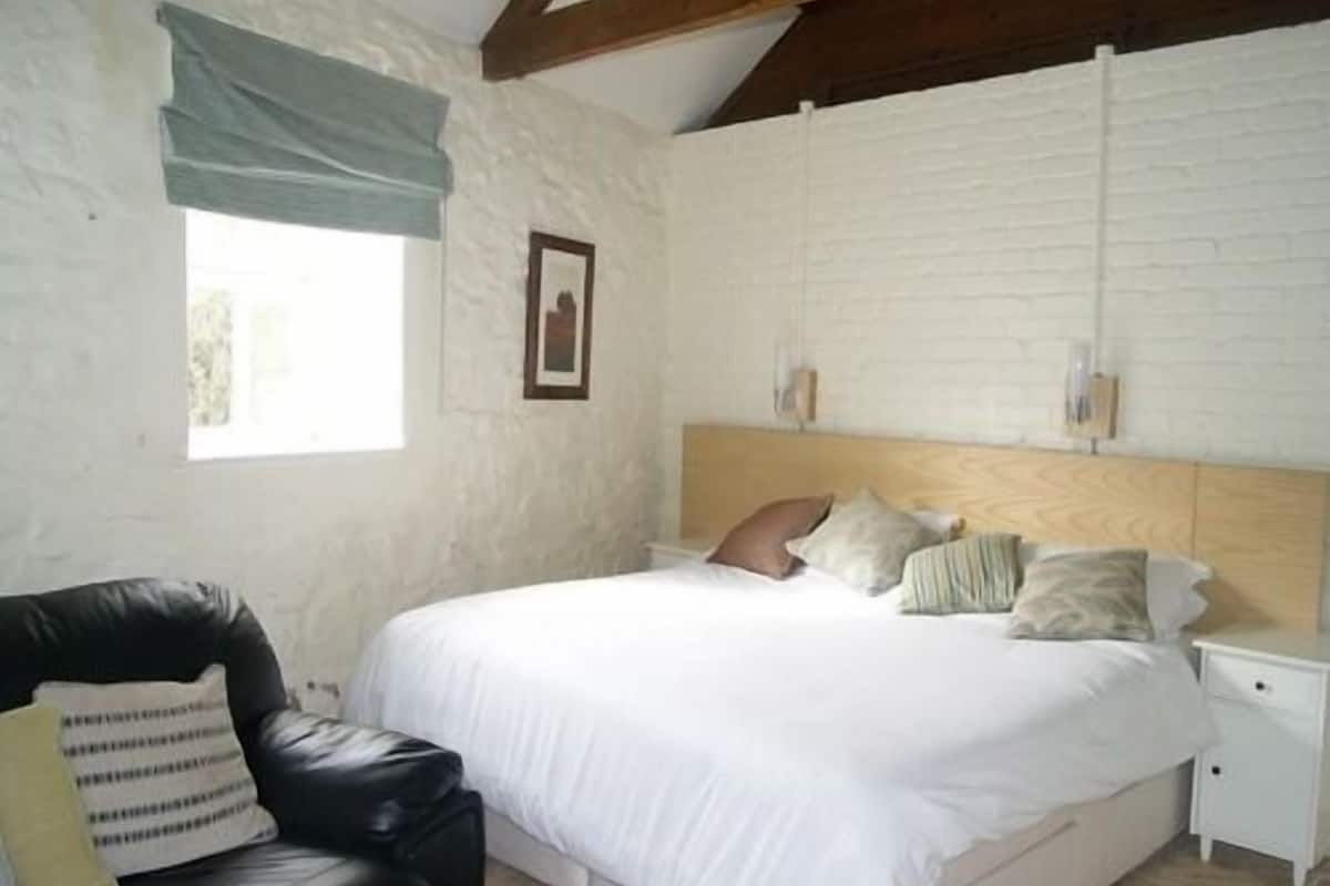 A bedroom with a bed, a nightstand, a chair, and a window with curtains.