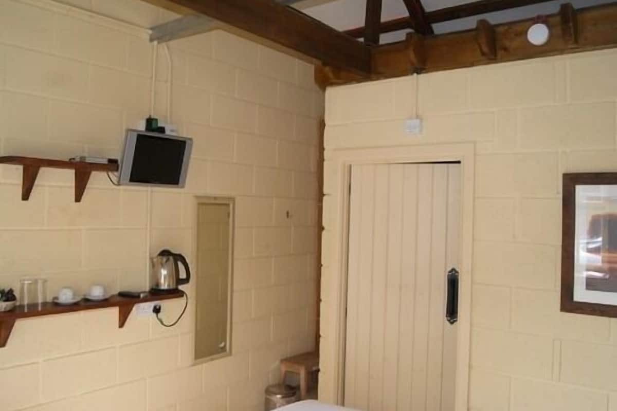A room with a bed, a wooden shelf with a television and cups, a door, and a small stool.