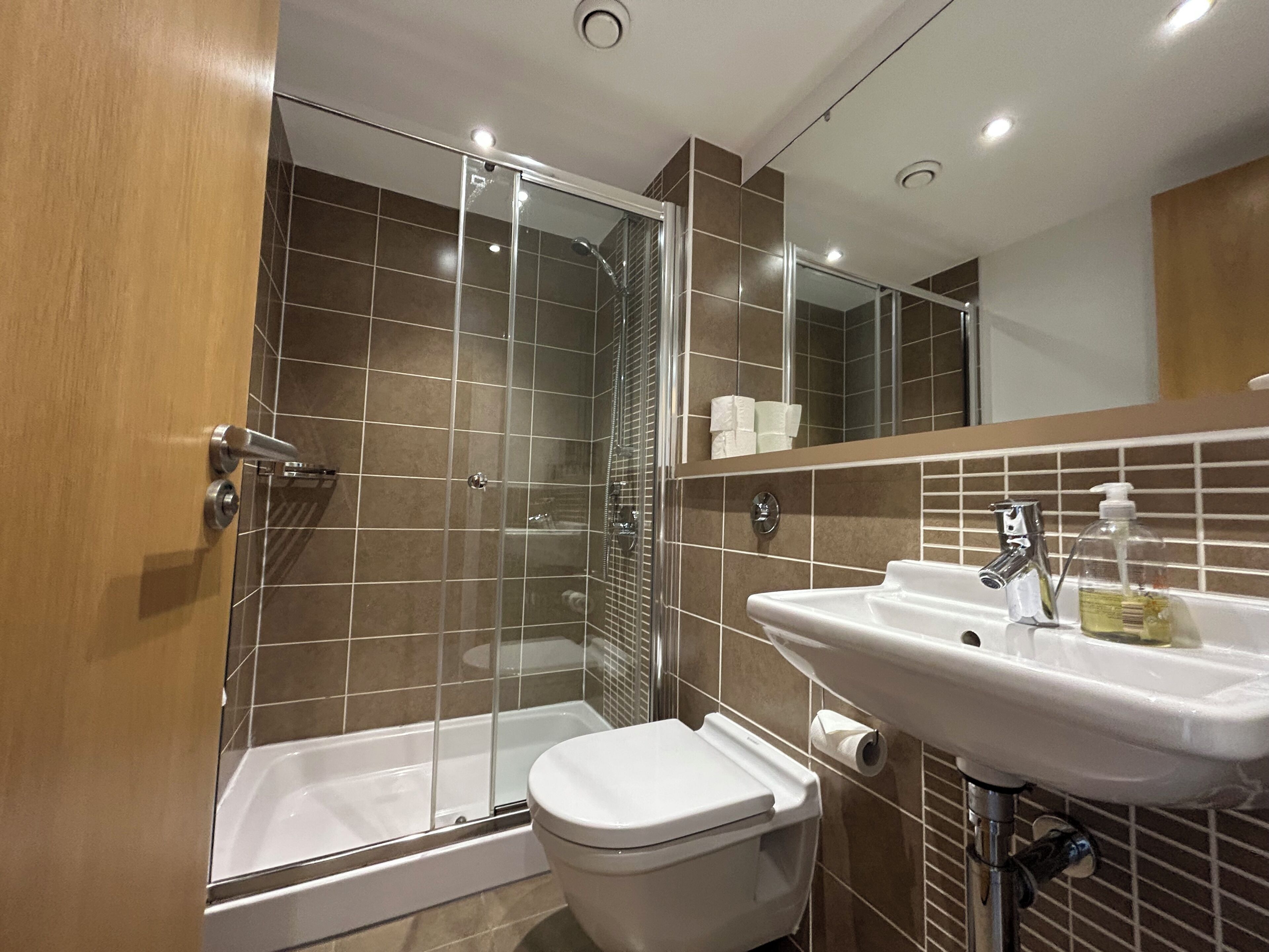 Une salle de bain équipée d’une douche, de toilettes, d’un lavabo et d’un miroir.