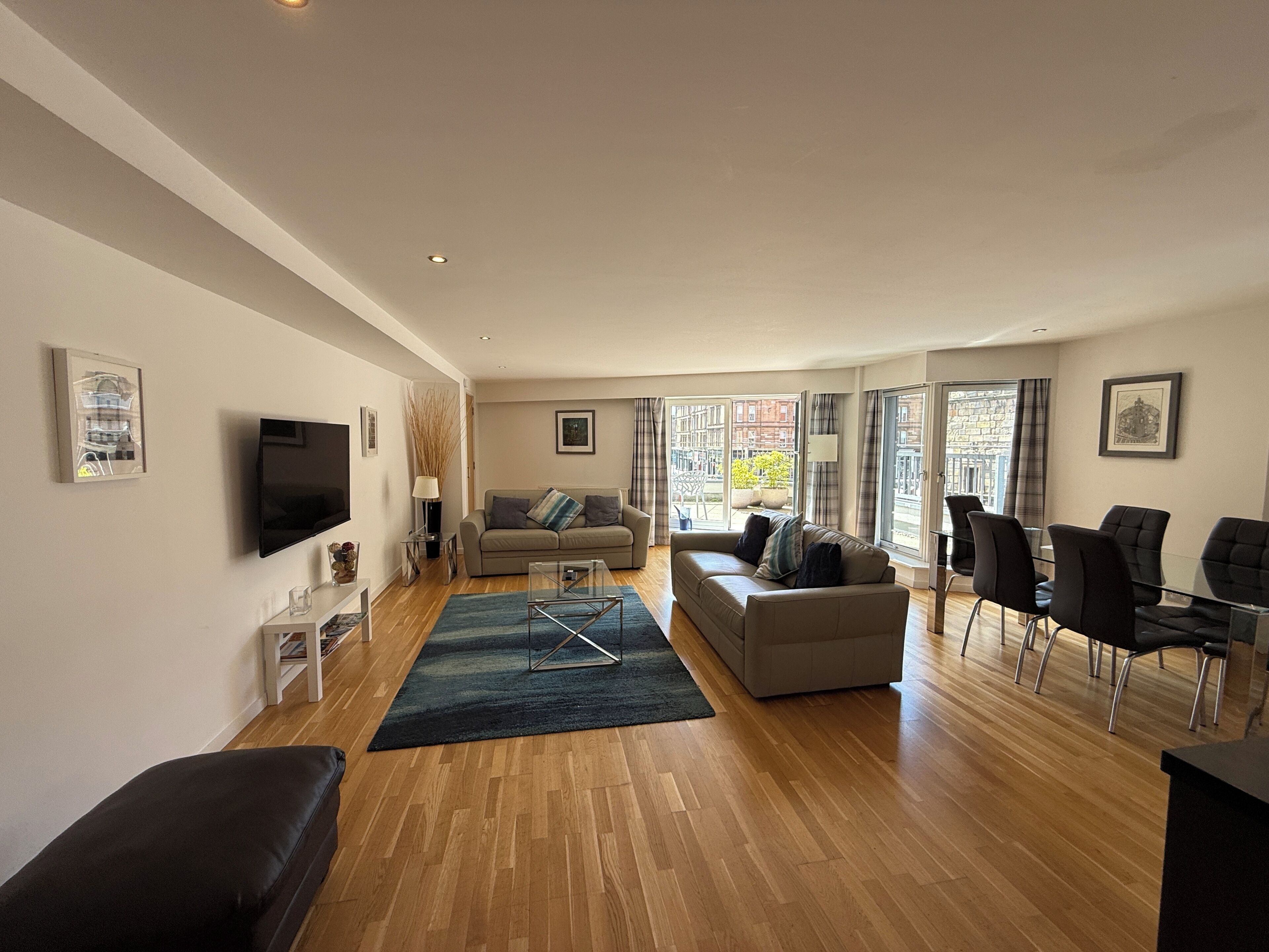 A spacious living room with a flat-screen TV, a sofa, a coffee table, and a dining area with chairs.