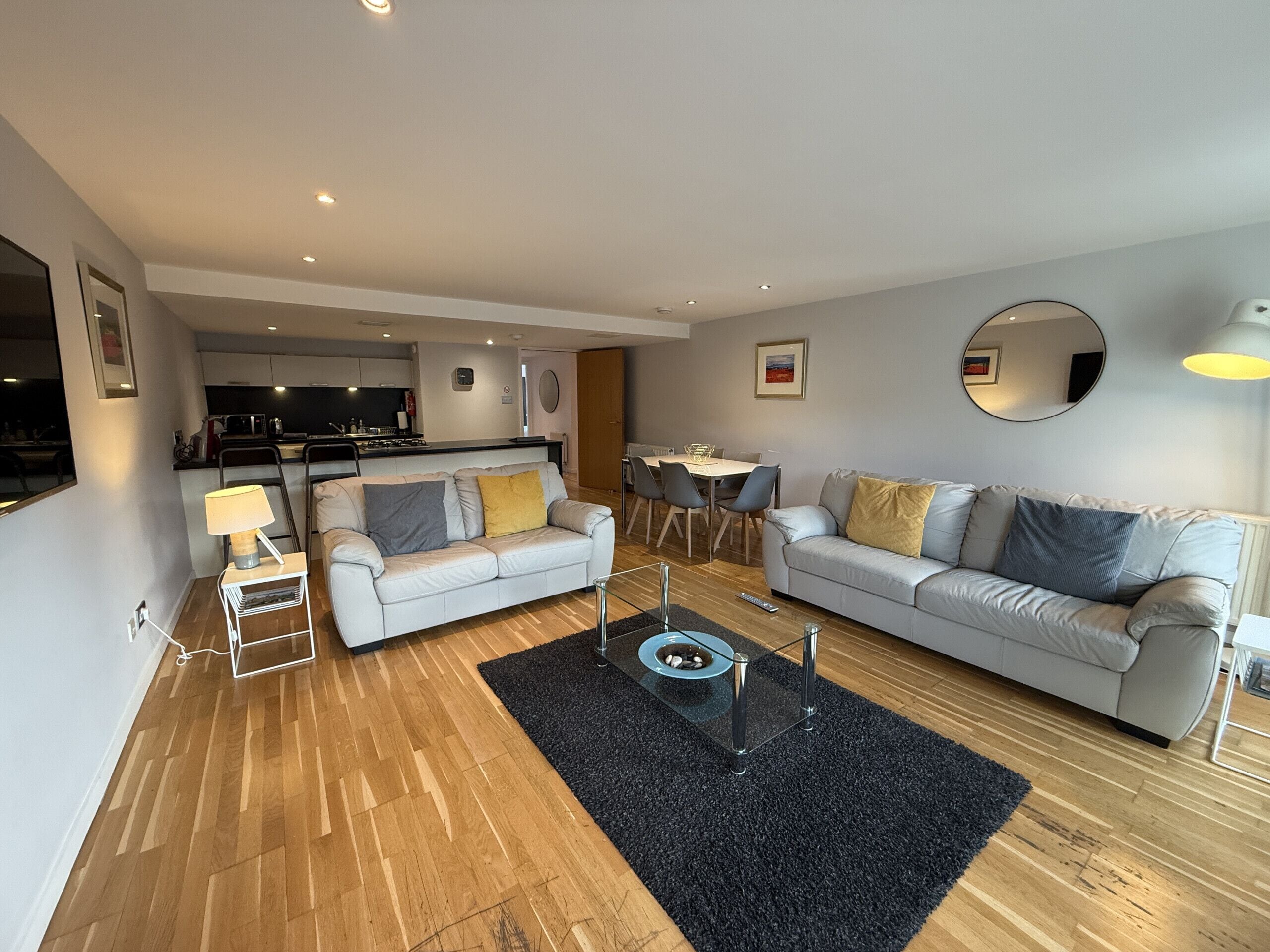 A modern living room with two sofas, a coffee table, a dining table, and a kitchen in the background.