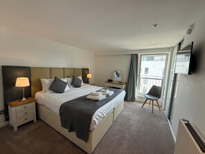 A hotel room with a bed, bedside tables, a desk, a chair, a TV, and a window with a view.