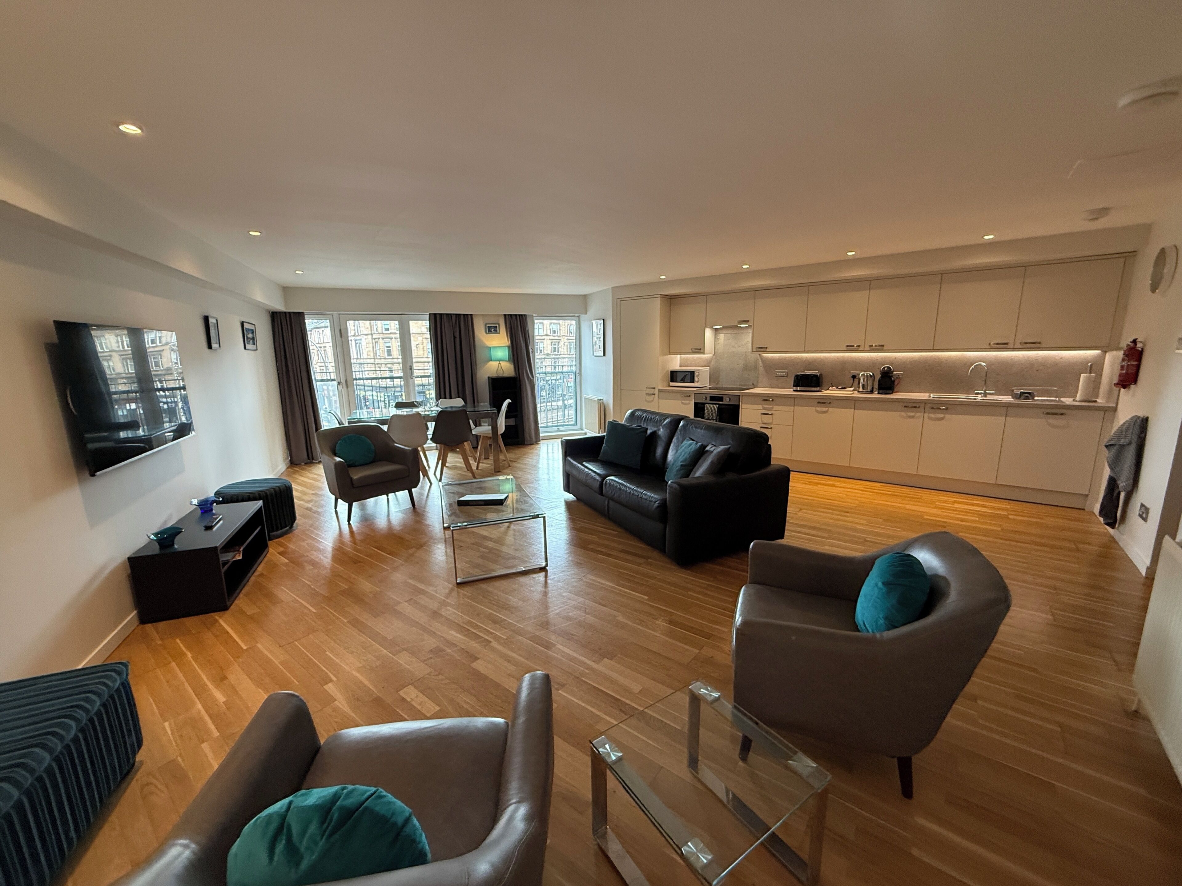 Una sala moderna con una televisión de pantalla plana, sofás de cuero, una mesa de centro de vidrio y un comedor con una cocina al fondo.