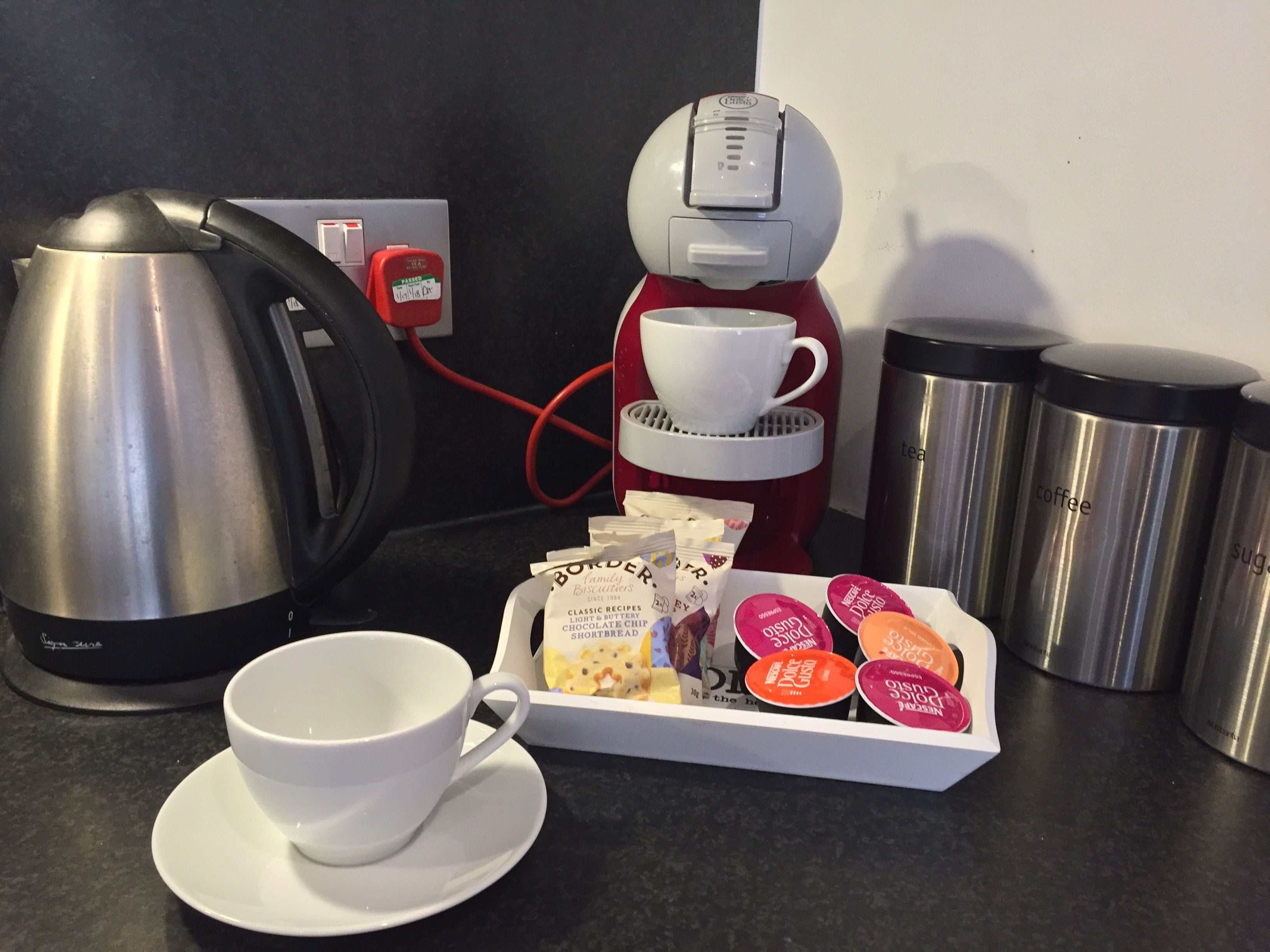A coffee maker, a kettle, a cup, a tray of biscuits, and a thermos.