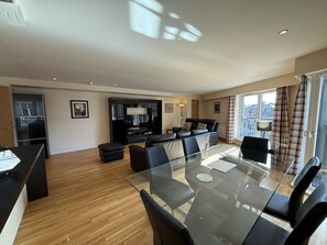 A modern living room with a glass dining table, black sofas, and a black entertainment unit.