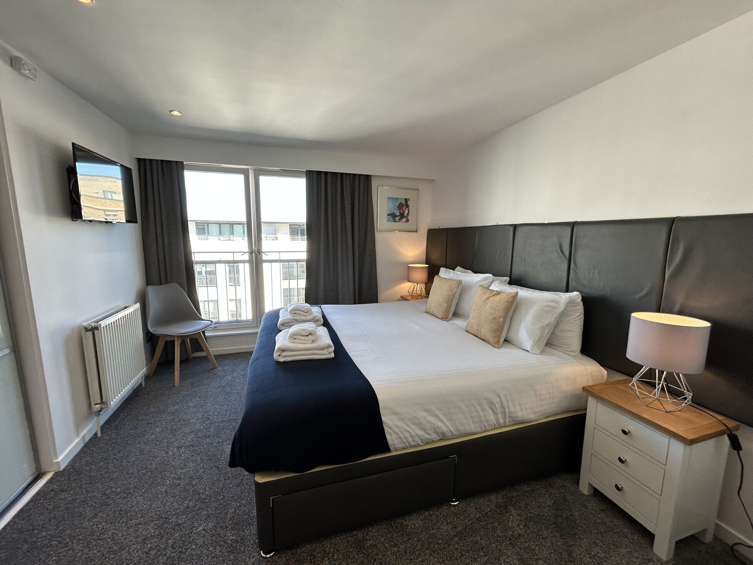 Quarto de hotel com cama, mesa de cabeceira, cadeira e vista para a cidade.