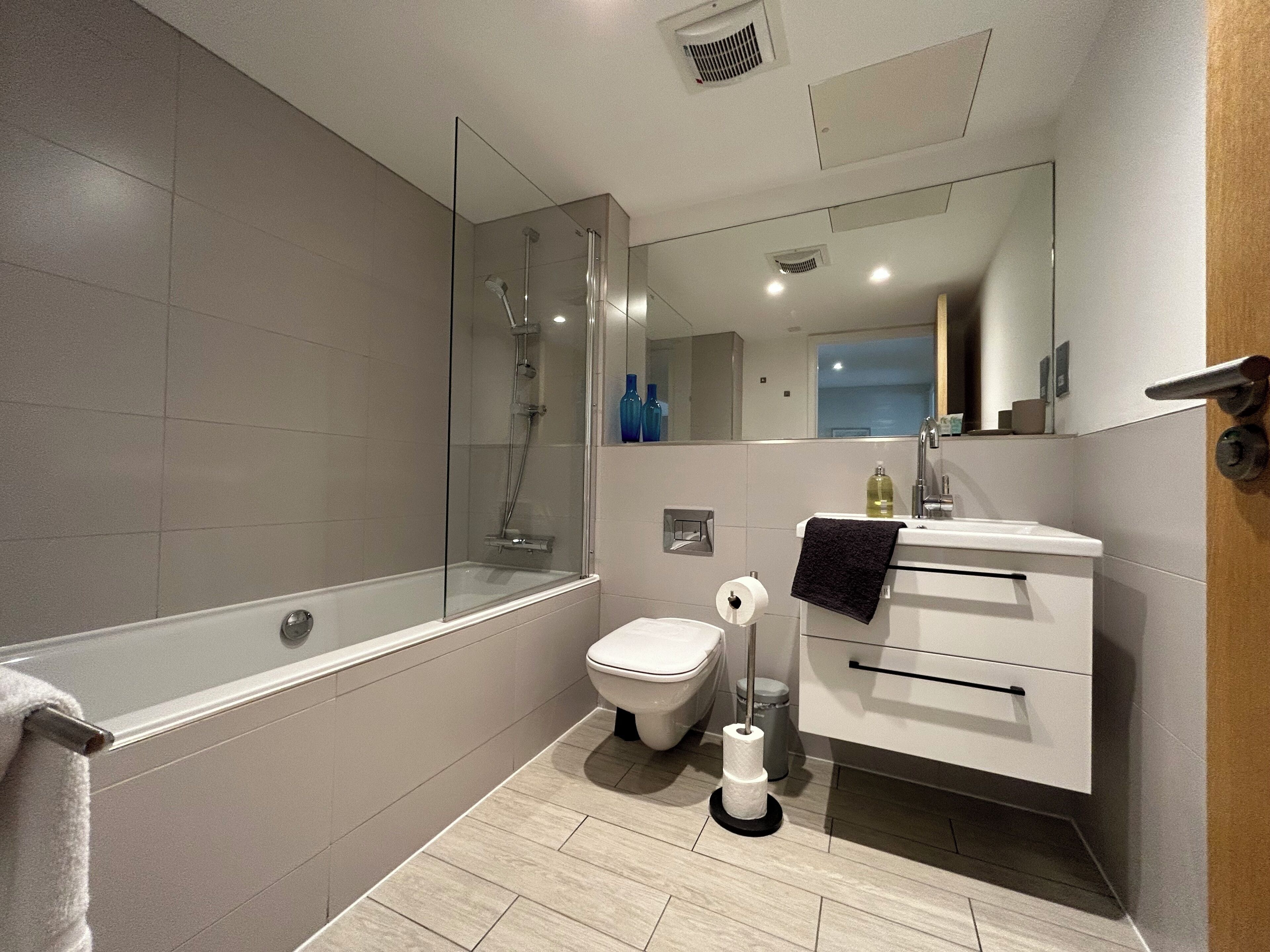 A modern bathroom with a glass-enclosed shower, a toilet, a sink with a towel, and a mirror.
