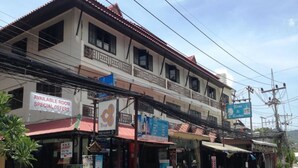 A two-story building with multiple shops on the ground floor. There is a sign for a room available with special offers. - Samui Beach Apartments (Koh Samui)