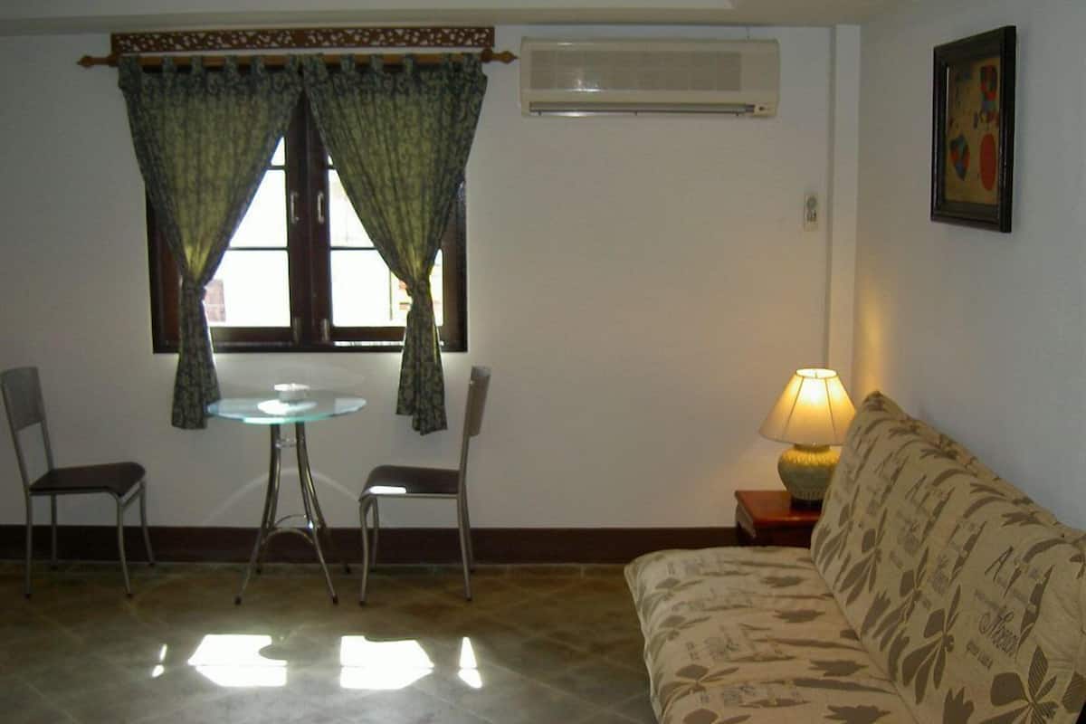 A living room with a glass table, two chairs, a sofa, a lamp, and a window with curtains.