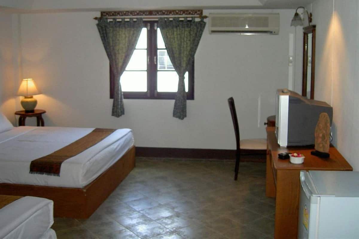 A hotel room with a bed, a desk with a television, a chair, a lamp, and an air conditioning unit.