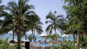 A poolside area with lounge chairs and umbrellas, palm trees, and a view of the ocean. - Samui Beach Apartments (Koh Samui)