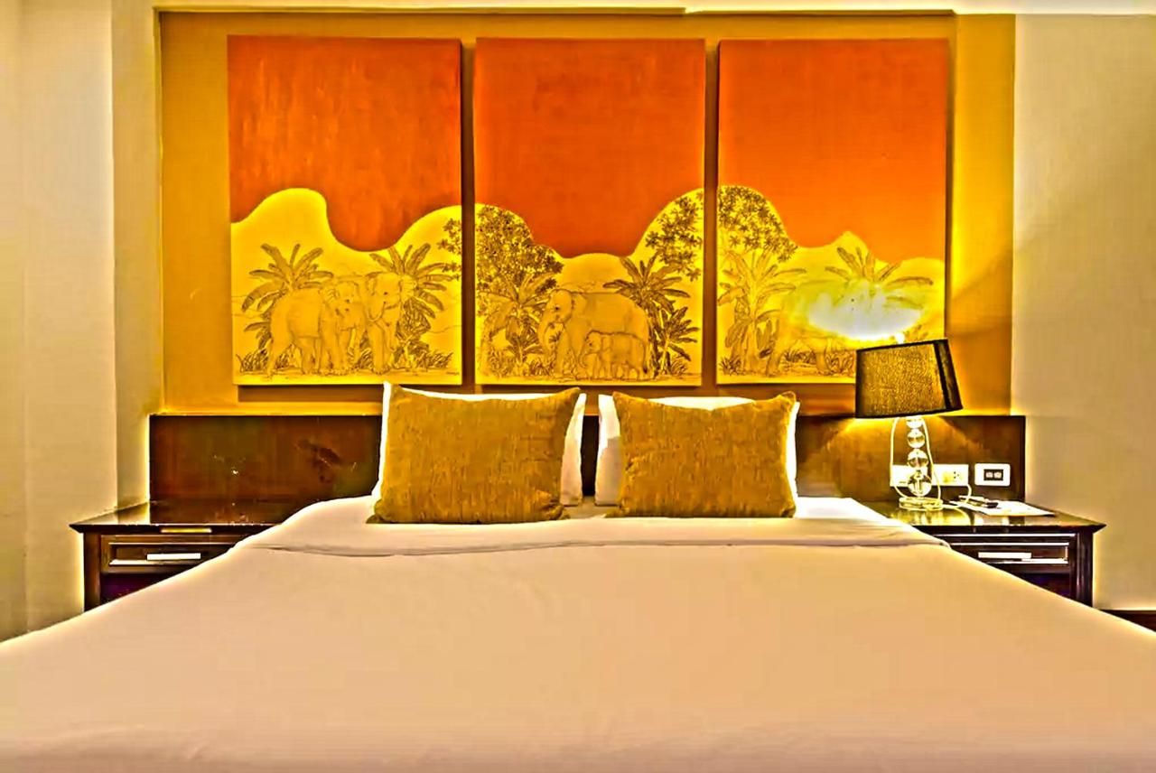 A hotel room with a large bed, two bedside tables, a nightstand, and a wall-mounted lamp.