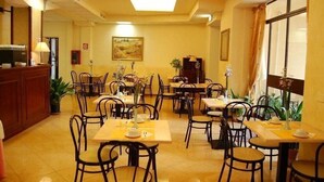 Un comedor de hotel con varias mesas y sillas, una recepción y un cuadro en la pared.