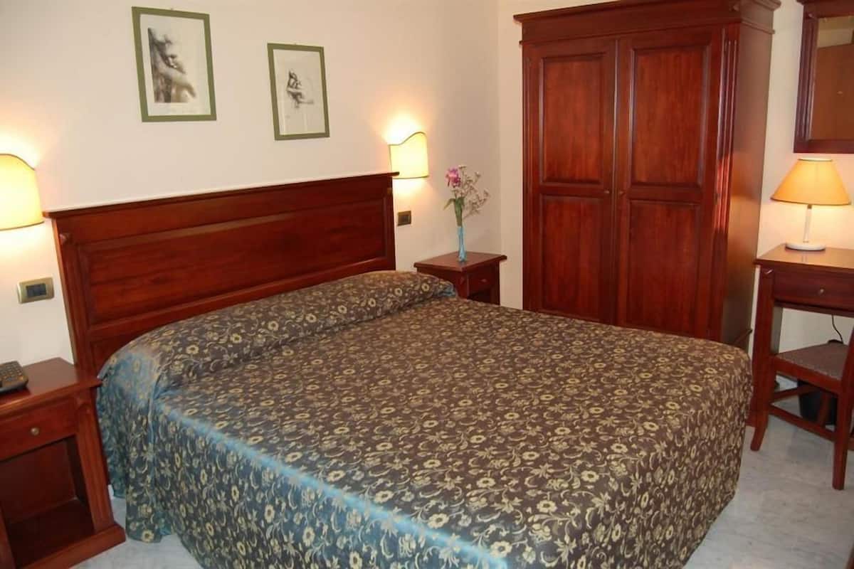 A bedroom with a double bed, wooden headboard, two bedside tables with lamps, a wardrobe, and framed artwork on the wall.