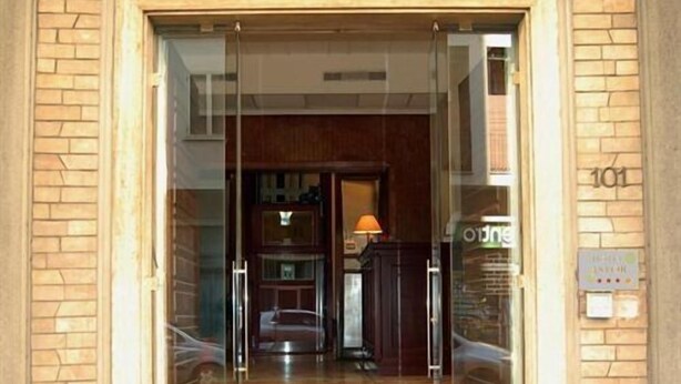 Entrada de un edificio con puerta de vidrio, fachada de ladrillo y un interior visible con un escritorio y una lámpara.