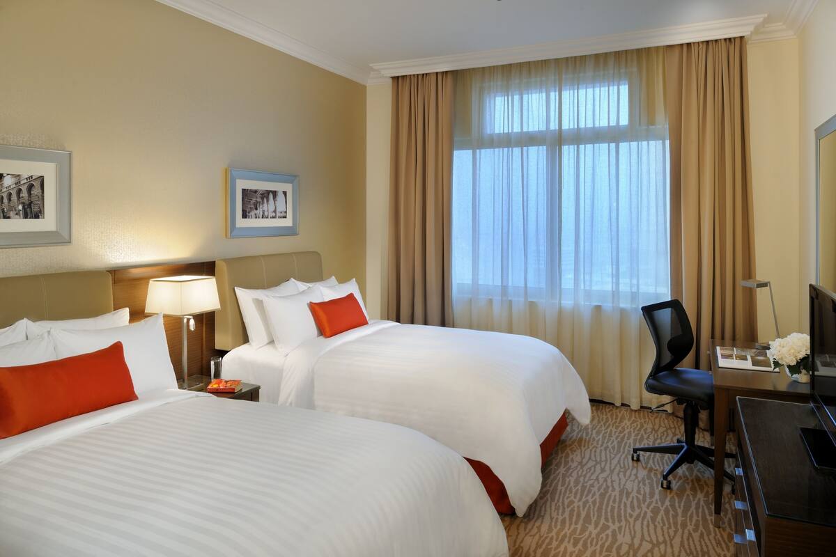 A hotel room with two beds, a desk, a chair, and a large window with curtains.