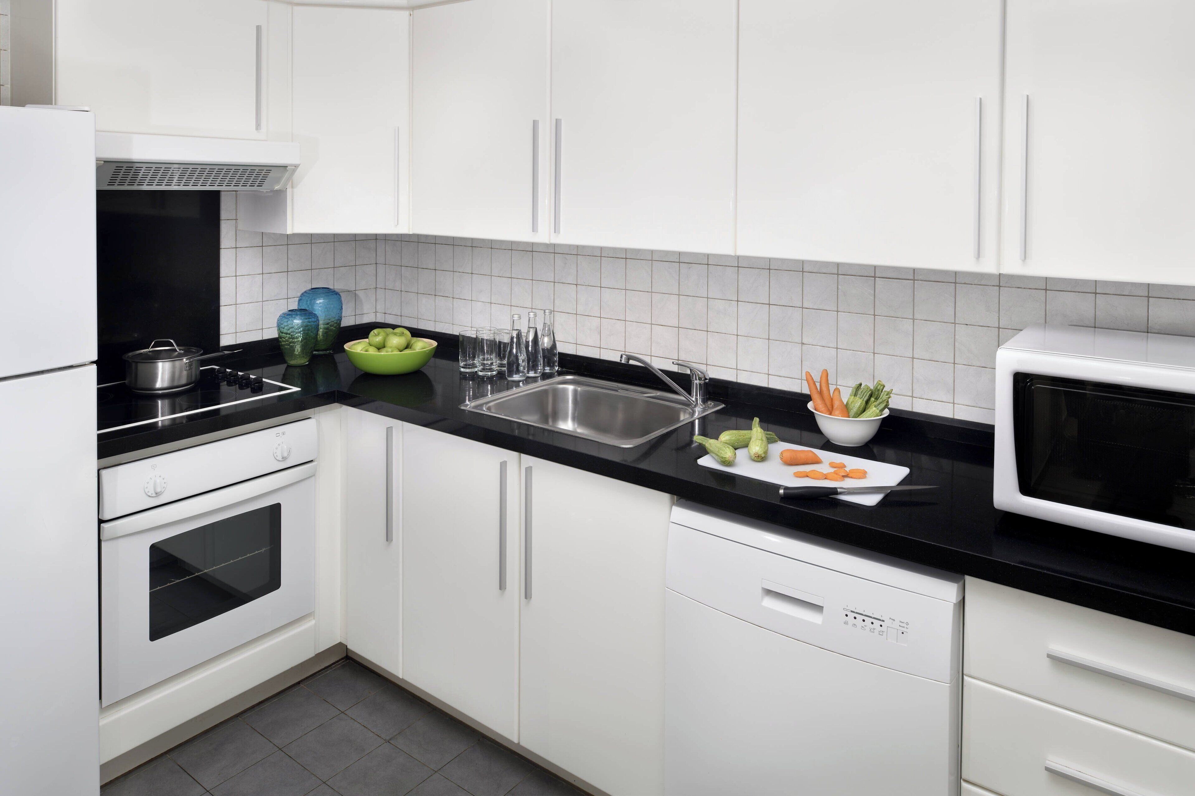 A modern kitchen with white cabinets, a black countertop, a stainless steel sink, and a microwave.