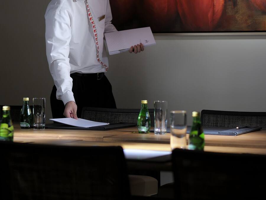 A person standing at a table with a name tag, holding a piece of paper, with a large floral painting on the wall behind them.