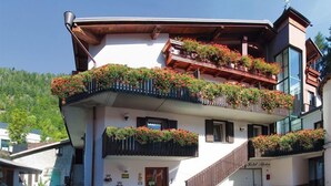 Un edificio de varios pisos con balcones decorados con plantas en macetas, una escalera que lleva a la entrada y un letrero que indica que es un hotel.