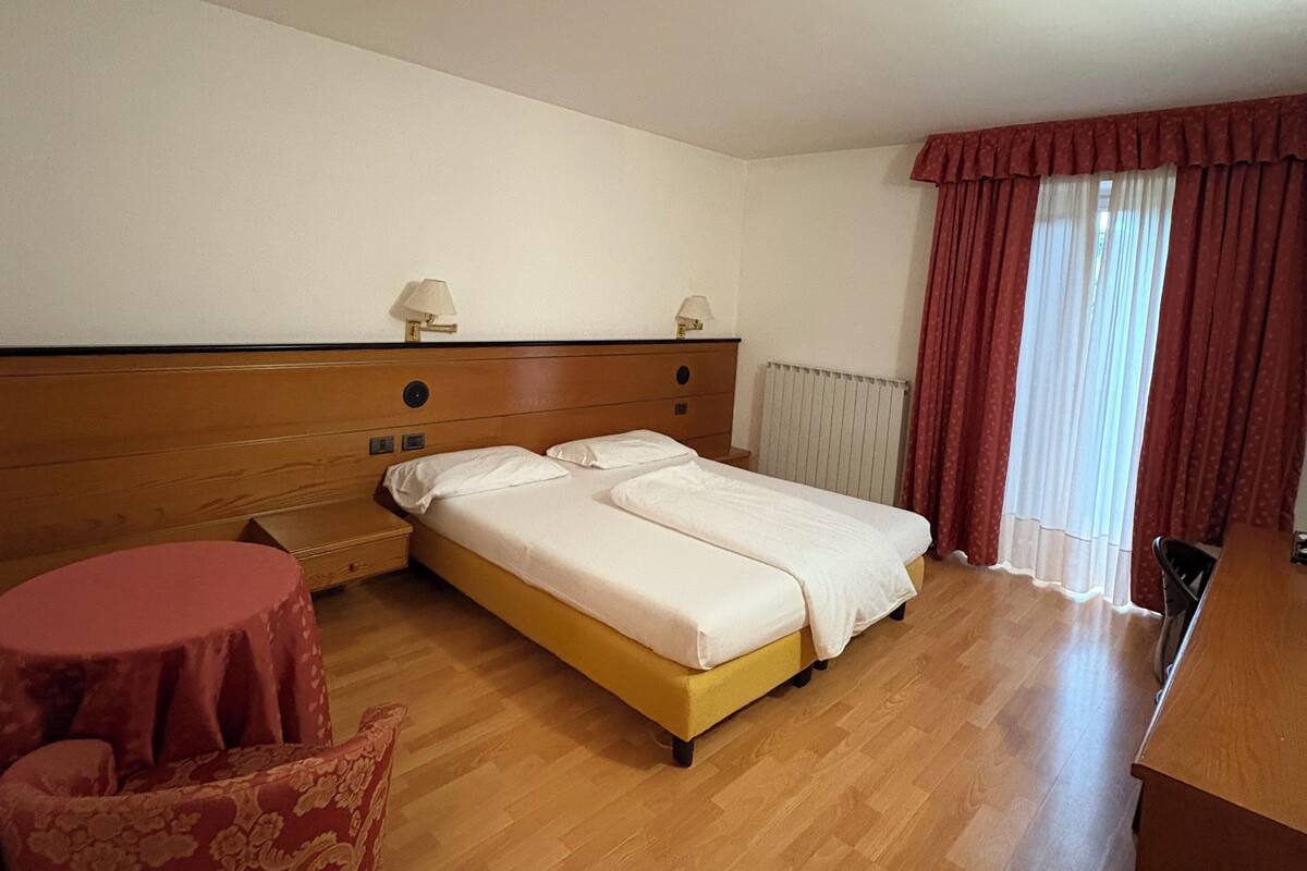 Ein Hotelzimmer mit einem Doppelbett, einem kleinen runden Tisch, einem rot gemusterten Sessel und einem Holzbüro.