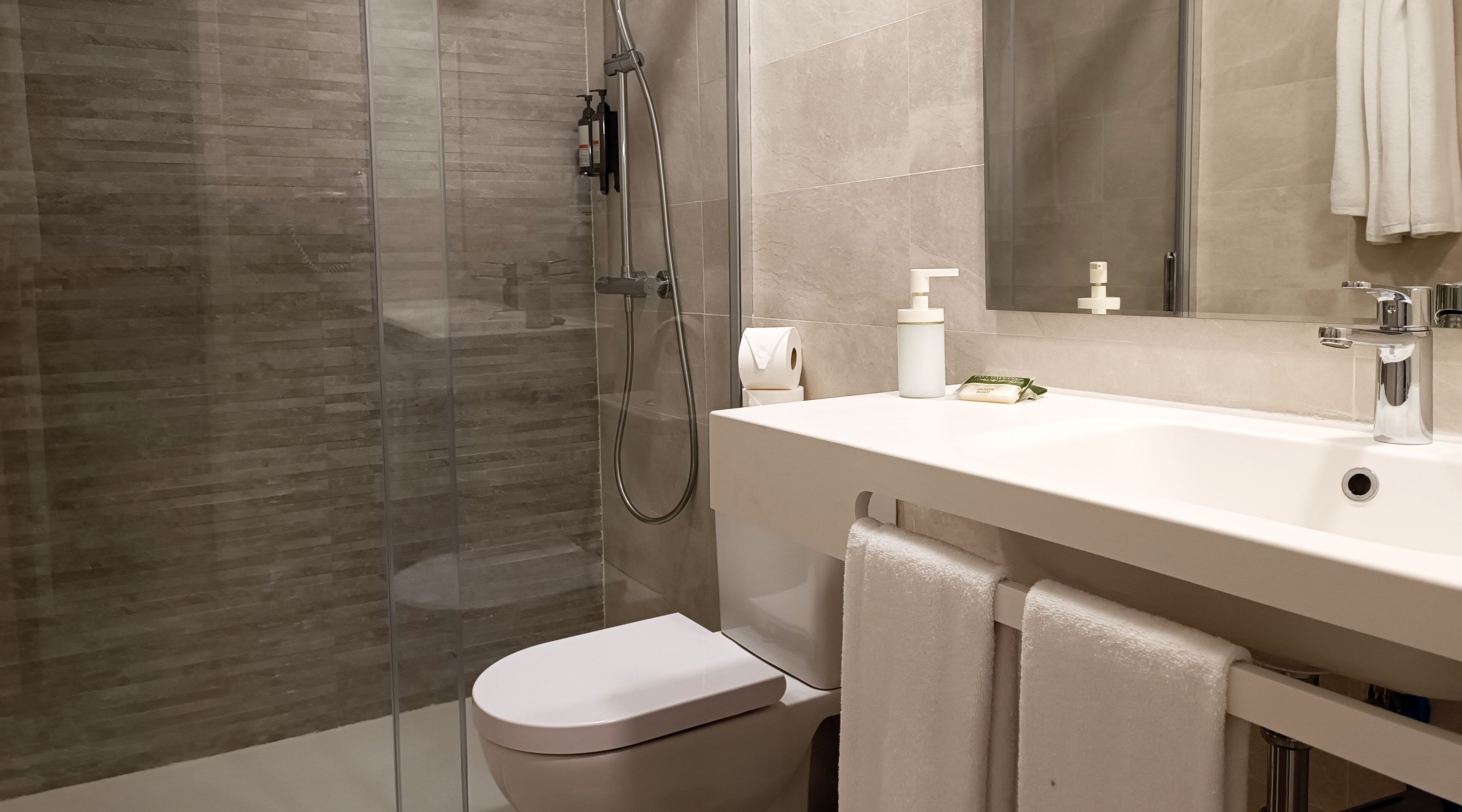 Un baño moderno con cabina de ducha de vidrio, un lavabo blanco y un inodoro.