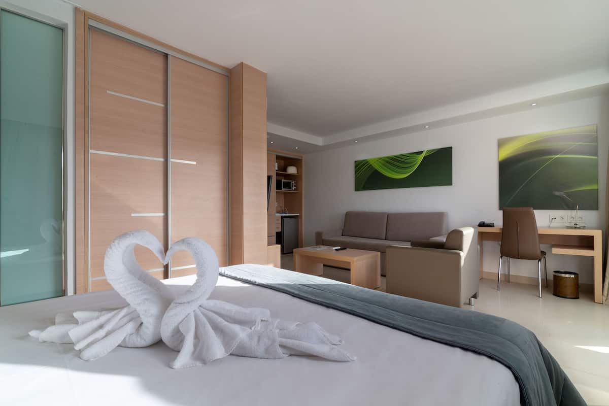 A modern hotel room with a bed, a desk, a sofa, and a wardrobe.