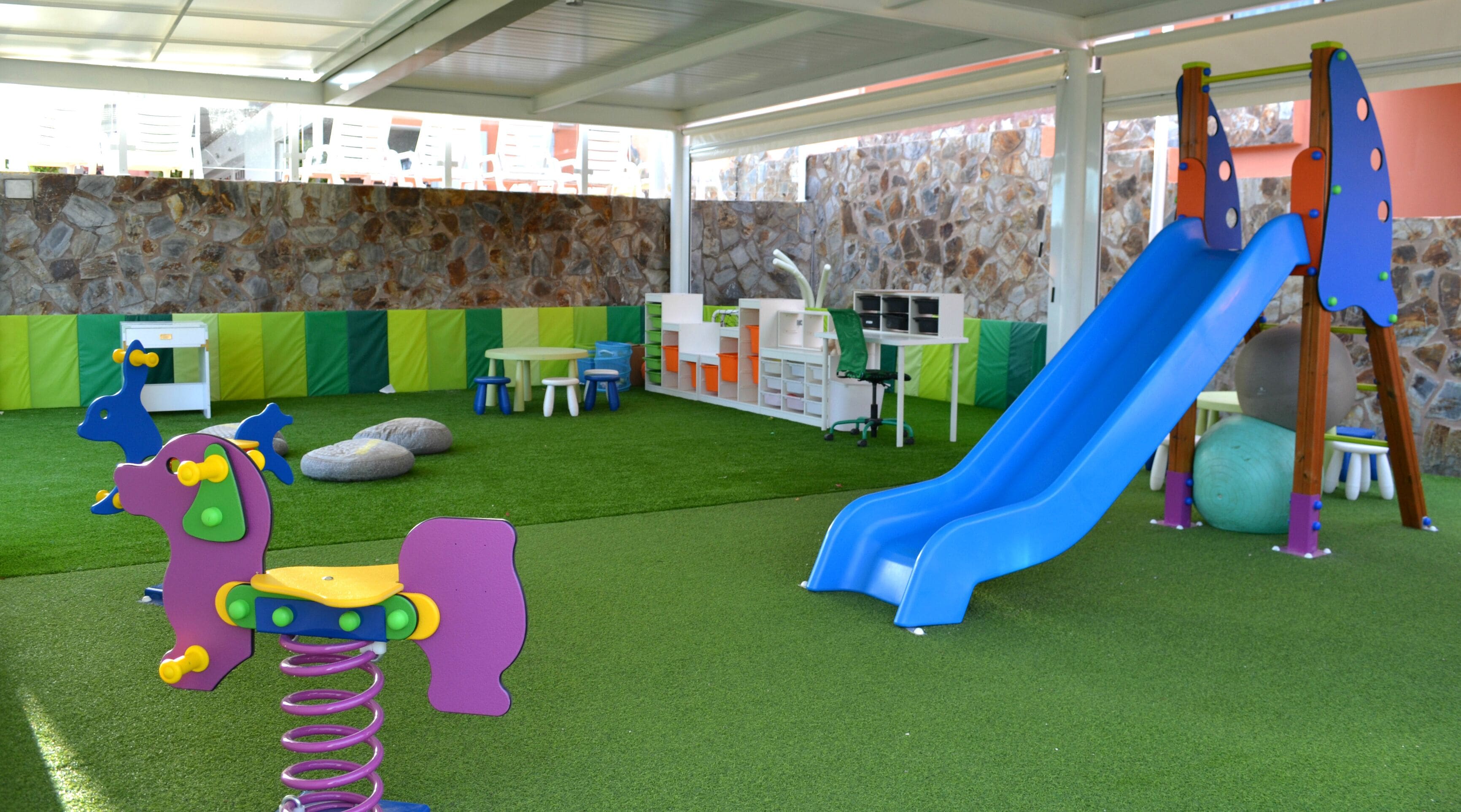 A children's play area with artificial grass, a blue slide, and various play structures.