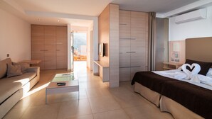 Ein modernes Hotelzimmer mit Sofa, Bett mit herzförmigem Handtuch, Fernseher und Minibar.