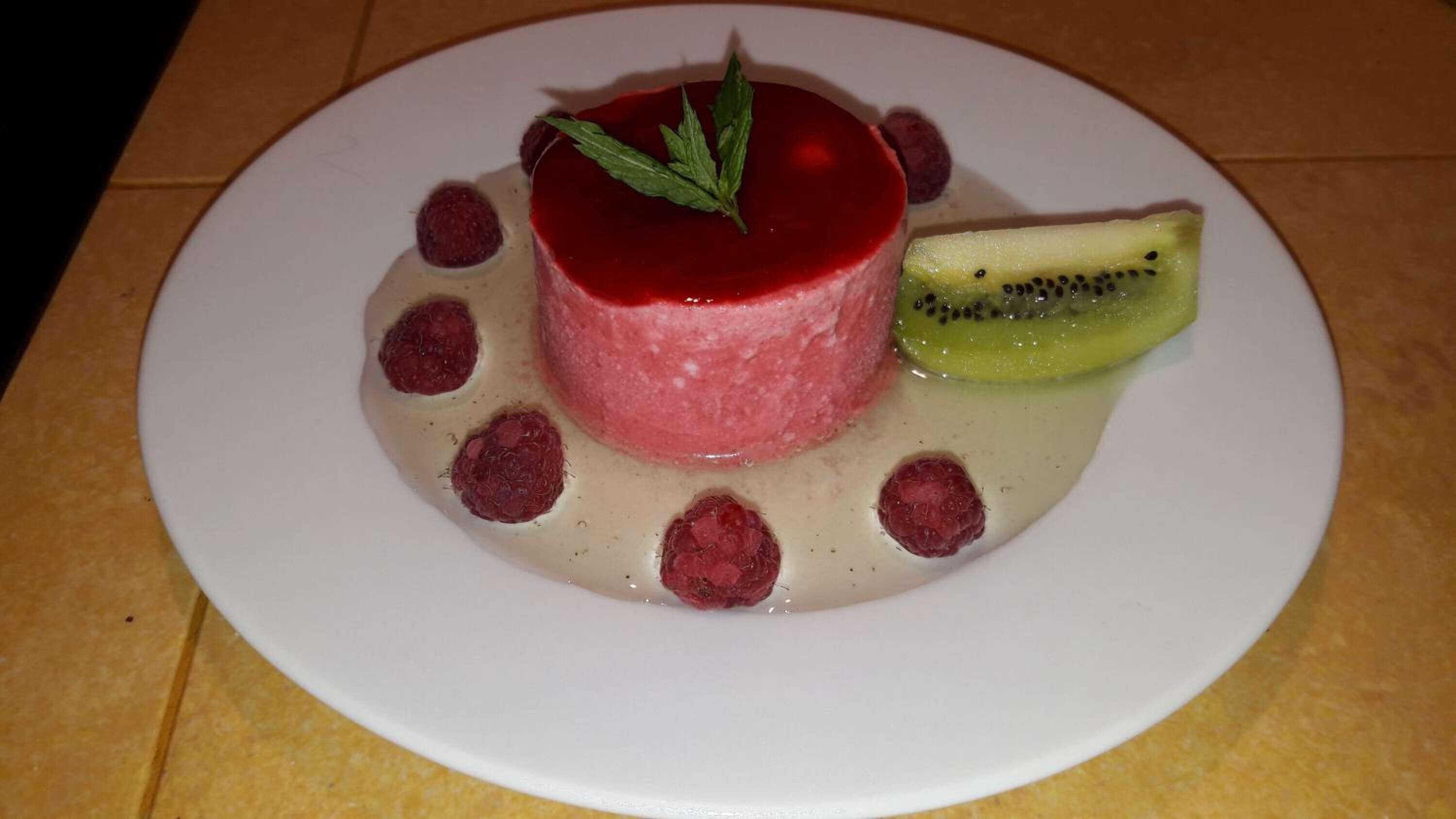 A dessert on a white plate with a red center, surrounded by raspberries and a slice of kiwi.