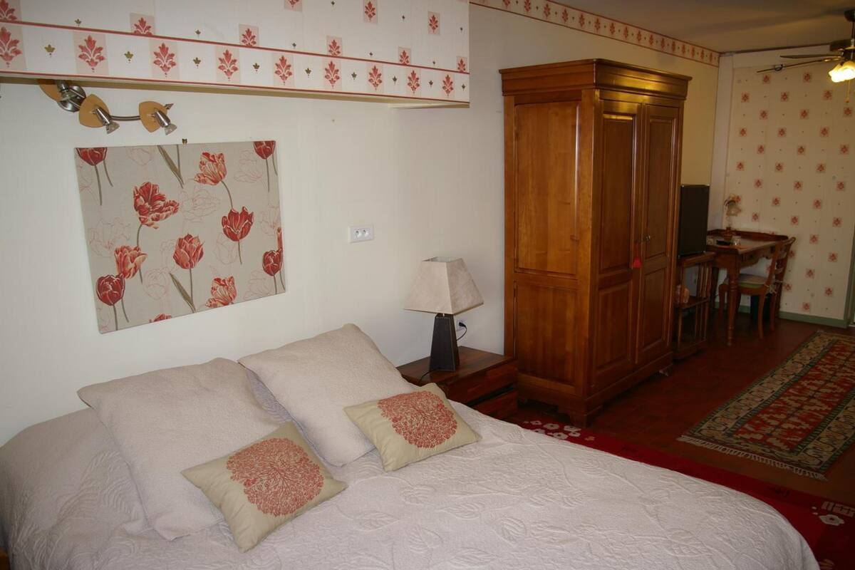 A bedroom with a bed, a wooden wardrobe, a desk with a chair, and a patterned wall.