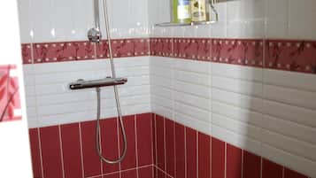 Un baño con azulejos blancos y rojos, una ducha con cabezal de ducha manual y un estante con artículos de tocador.