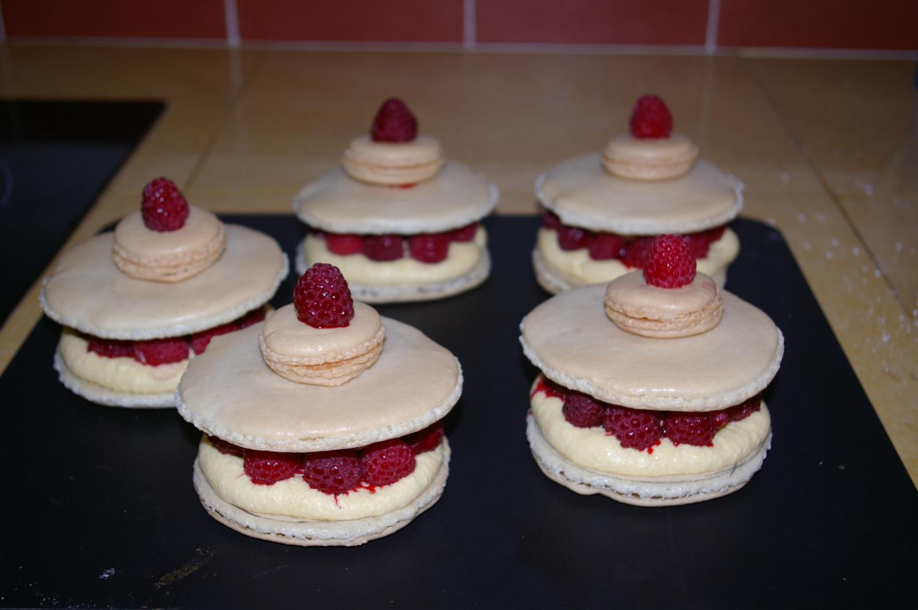 Six dessert items with raspberry and cream layers, arranged on a black surface.