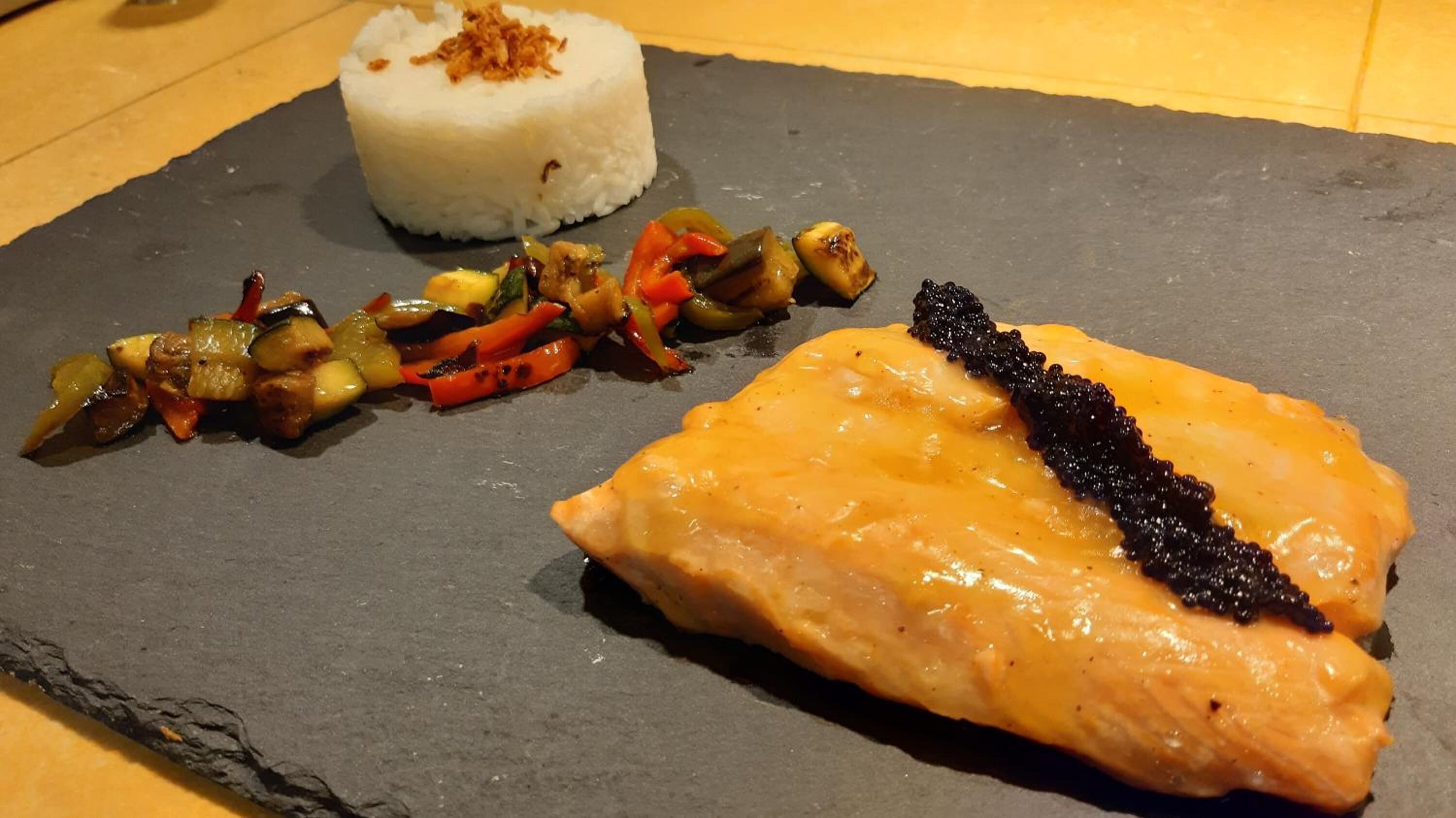 A meal consisting of salmon, rice, and a vegetable medley on a slate plate.