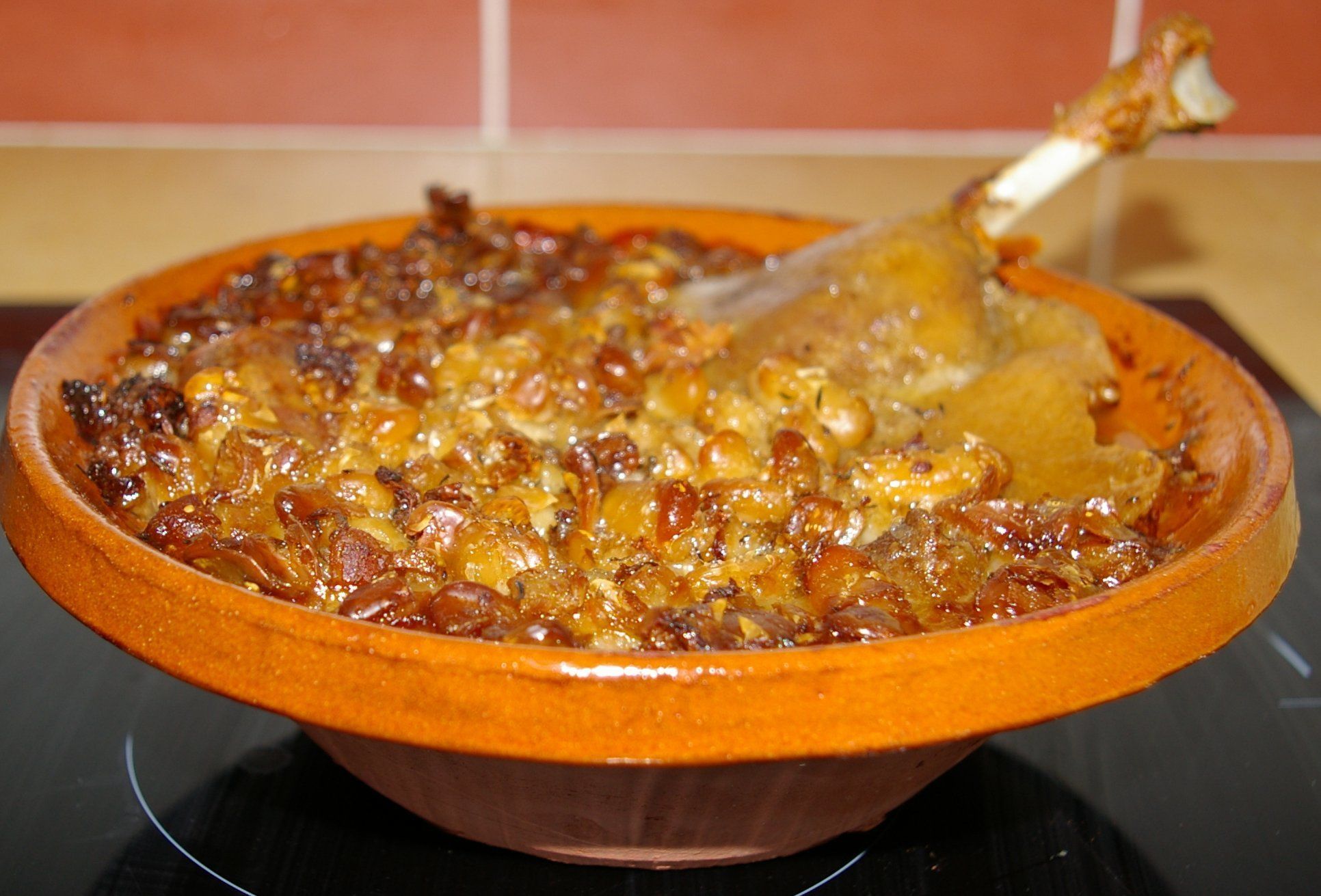 Un plat en céramique contenant un plat cuit au four, de couleur brun doré, et qui semble contenir de la viande et des légumes, le tout posé sur une surface sombre.