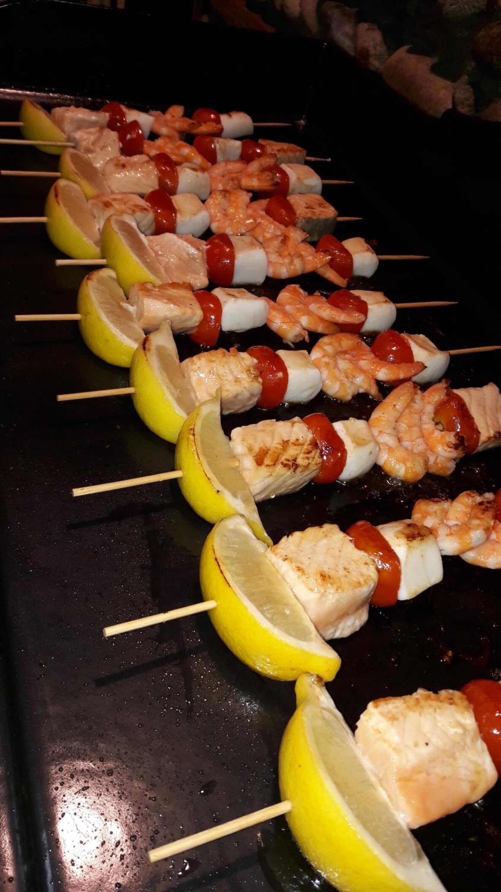 Skewers of grilled chicken, shrimp, and cherry tomatoes on a grill.
