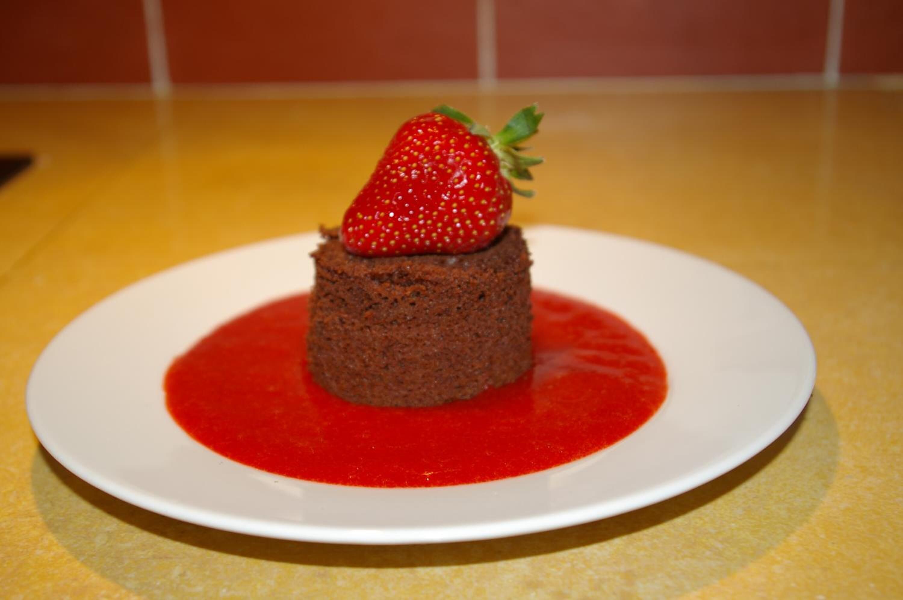 A dessert on a white plate with a red sauce and a strawberry on top.
