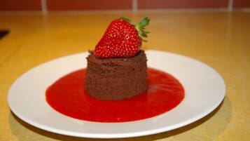 A dessert on a white plate with a red sauce and a strawberry on top.