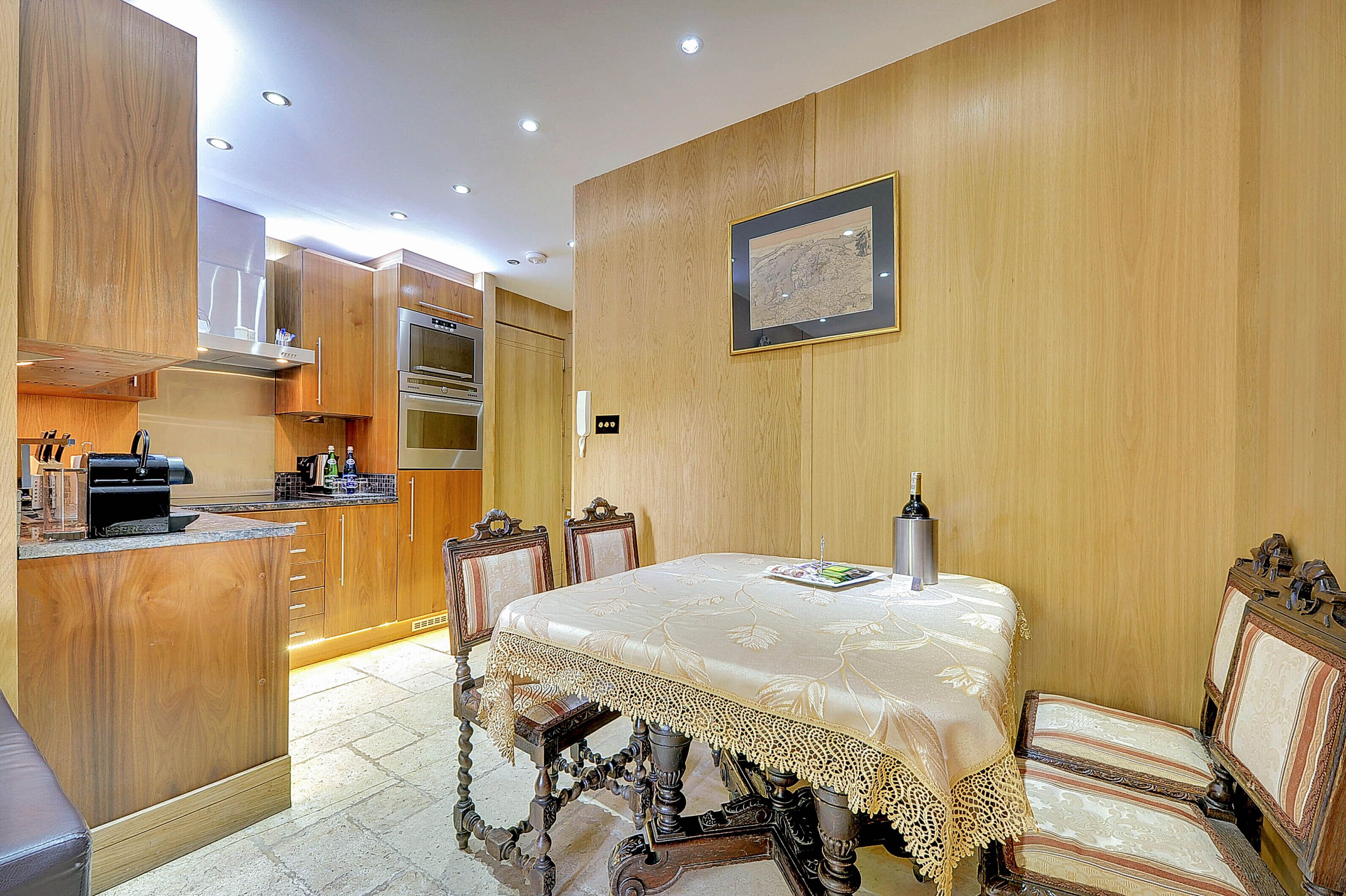 A dining area with a table set for two, wooden cabinetry, and a modern kitchen in the background.