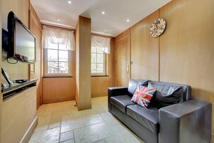 A modern living room with a leather sofa, a flat-screen TV, wooden paneling, and a clock on the wall.