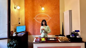 Un mostrador de recepción con un cartel que dice 'RECEPTION', un monitor de computadora, una planta y una caja registradora.