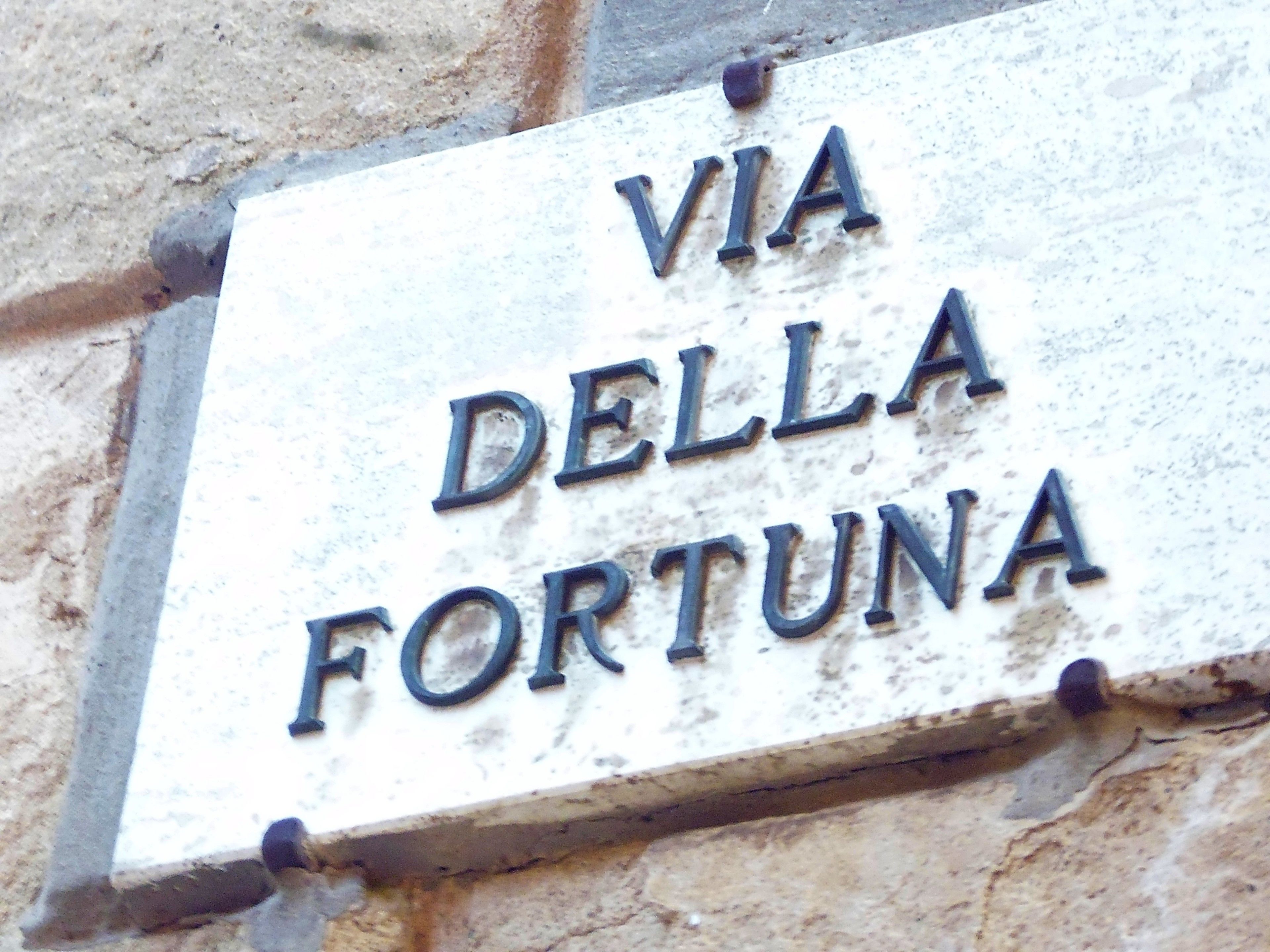 Un letrero con el texto "VIA DELLA FORTUNA" sobre una pared de piedra.