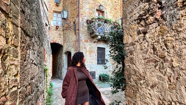 Un estrecho callejón con paredes de piedra y suelo de ladrillo, que conduce a un edificio con ventanas y balcones.