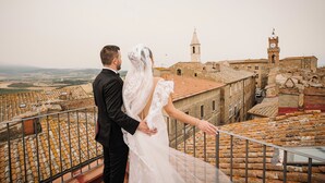 Una pareja en un balcón con vista a un pueblo histórico de tejados de terracota y una imponente torre del reloj.